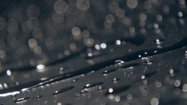 在慢动作爆裂的水滴中流动的多雨水流在慢动作中神奇的宏观镜头 在粗糙的黑色表面上的雨点中扭动着薄薄的 它产生艺术和梦想的心情 — 图库视频影像