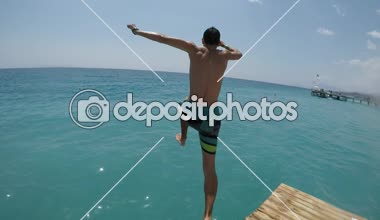Güneşli bir yaz aylarında güneşli bir günde Kızıldeniz celeste dalgaları ahşap bir platformdan dalış uzun şortlu genç bir brunet adam neşeli görünümünü Mısır'daki bir ahşap platform üzerinden atlama cesur genç adam