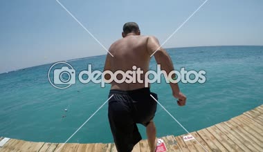 Etkin adam çalıştıran ve ayak ilk bir platformdan yaz koşma ve ayak ilk mutlu Mısır'daki Red Sea'deki/daki ahşap bir platformdan yaz aylarında güneşli bir atlama cesur biri neşeli görünümünü Kızıldeniz'dalış.