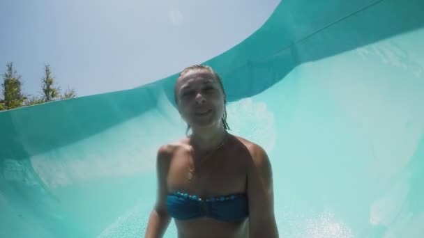 幸せな陽気な女下に乗って 夏の晴れた日にトルコのアクアパークで青色の長いチューブを滑り落ちるビキニで笑顔の金髪女性のトルコ陽気な眺めのアクアパーク Selfie — ストック動画
