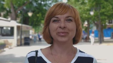 Ayakta ve yeşil bir sokakta gülümseyen güneşli bir günde bir gülümseyen sarışın kadının iyimser görünümü bob saç kesimi içinde duran ve güneşli bir yaz aylarında yeşil bir sokakta gülümseyen çizgili bir bluz ile neşeli sarışın kadın 