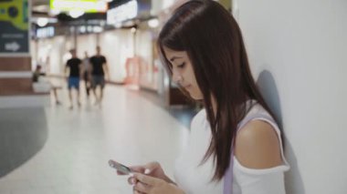 Bir alışveriş merkezinde yaz Amazing profil net, havadar bir alışveriş merkezinde onun smartphone cep telefonu ile mesaj yaz aylarında tarama şık beyaz elbiseli güzel bir kızın onun smartphone üzerinde net sörf çekici esmer kız.