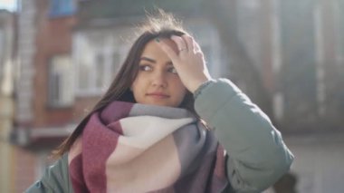 Güzel kız bir fantezi eşarp ve saçlarını sırayla koyarak ve bir kenara slo-mo sokakta merak ile seyir moda giysiler içinde güzel bir kadının slo-mo romantik görünümünde kışın bir sokakta smartening ceket