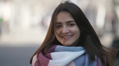 Mutlu kız modaya uygun eşarp ve yavaş hareket neşeli bokeh portre bir güzel kız kış moda çizgili Fularlı uzun saçlı parkta gülüyor ceket ve ayakta ve slo-mo arka sokakta gülüyor ceket