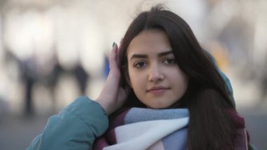 Saçlarını sırayla koyarak ve slo-mo kışın güneşli sokakta hayattan zevk modaya uygun giysiler içinde güzel bir kadının slo-mo etkileyici bokeh görünümünde kışın bir sokakta smartening bir fantezi Fularlı Glamour kız