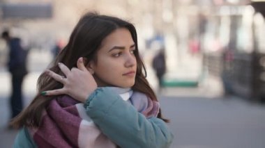 Yün, ipek bir eşarp kış slo-mo güzel bokeh görünümünde zarif bir genç kadının modaya uygun giysiler sipariş ve bir kenara slo-mo kışın güneşli sokakta arıyor saçlarını koyarak bir sokakta smartening şık esmer kız