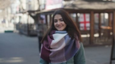 Gidiş ve uzun bağsız kıl ayakta ve slo-mo kışın bir sokakta gülümseyen şık eşarp ile mutlu bir esmer kız harika manzarasını yavaş çekimde bir sokakta gülümseyen şık giysileriyle tatlı hatun