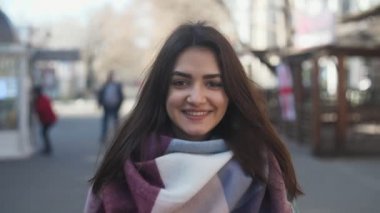 Gülümseyen ve yavaş çekimde bir sokakta duran ve slo-mo kışın bir sokakta gülümseyen moda giysiler içinde uzun bağsız kıl ile mutlu esmer kız olumlu görünümünü ayakta vogue Fularlı güzel kız