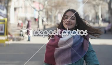 Gülümseyen ve başını bir sokakta uzun bağsız kıl gülümseyen bir kızla harika manzarasını slo-mo içinde ayakta ve saçlarını slo-mo kışın bir sokakta sallayarak çizgili Fularlı sallayarak çizgili Fularlı güzel kız