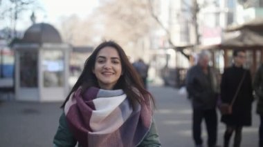 Modaya uygun giysiler bir cadde boyunca ağır çekim duygusal mutlu kız görünümünü kışın uzun bağsız kıl gülümseyen ve slo-mo kışın insanlarla bir cadde boyunca yürüme zarif bir eşarp ile gidiş neşeli genç kadın