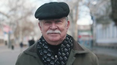Mutlu emekli adam ayakta ve düz bir kapak ve ayakta ve mutlu bir şekilde slo-mo kışın bir sokakta gülümseyen bir ceket bıyıklı bir gülümseyen kıdemli adamın slo-mo neşeli görünümünde bir sokakta gülümseyen bir bıyıklı
