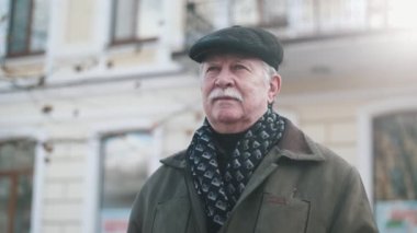 Komuta sizde ayakta ve düz bir kapak, sıcak ceket ve slo-mo Kışın açık havada duran bir örme eşarp bıyıklı beyaz saçlı bir adam etkileyici manzara yavaş çekimde bir sokakta etrafa bıyıklı 