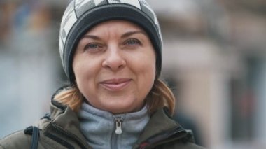 Sonbahar yavaş çekimde bir gülümseyen neşeli görünümü sarışın kadın örgü şapka, sıcak bir ceket ve sportif bir takım elbise, slo-mo sonbaharda bir sokakta duran bir sokakta gülümseyen örme şapka içinde mutlu sarışın kadın