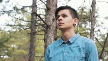 Neşeli brunet adam slo-mo baharda güneşli bir günde bir çam ormanında yürüyüş aşağı mavi gömlek, kahverengi pantolon ve spor ayakkabı bahargüneşli bir günde eski çam ormanında yürüyüş mutlu bir genç adamın görünümüaşağı