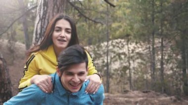 Mutlu esmer kız slo-mo bir çam ormanında doğru oturan uzun gevşek saçlı bir güle güle güle genç kadının görünümü slo-mo baharda bir köknar ormanda erkek arkadaşının arkasında oturan