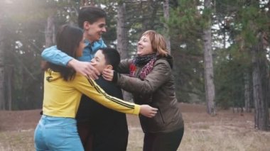 Neşeli aile eğlenceli ve slo-mo slo-mo güzel görünümünde çam ağacı çim birbirlerini kucaklayan, onun iki oğlu, ve mutlu bir kız oynarken ve slo-mo baharda bir çam ormanı çim birbirlerine sarılma