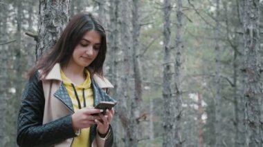Neşeli esmer kız slo-mo Pan ilkbaharda onun akıllı telefon net sörf ve slo-mo ilkbaharda köknar ahşap mutlu gülümseyen genç bir çekici kadın çekim köknar ahşap onu telefon net tarama