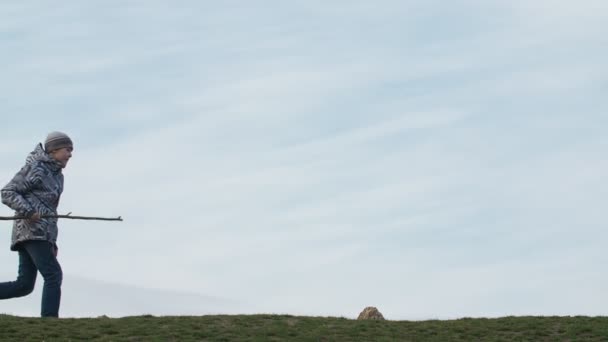 청바지와 모자에 쾌활한 아이의 Slo 프로필에 하늘과 잔디밭에서 막대기로 슬로우 — 비디오