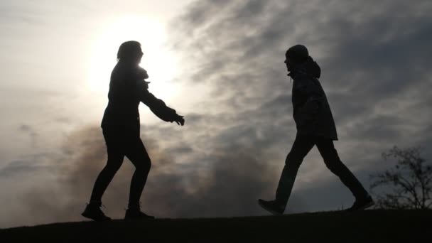 Petit garçon allant et sautant sur sa mère étreignant et gardant dans les silhouettes émouvantes d'une mère joyeuse dans une veste gardant ses mains de côté, attrapant son garçon qui marche, et l'élevant par temps nuageux dans les environs de 