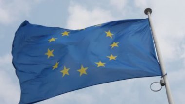 Avrupa Birliği bayrağı, ilkbaharda güneşli bir günde havada ciddi bir şekilde dalgalanıyor Yaz aylarında güneşli bir günde gururla havada sallanan Avrupa Birliği bayrağının manzarasına kadar. Gökyüzü göksel ve bulutlu.