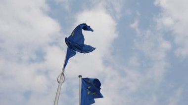Baharda Belçika'da açık mavi ve beyaz havada dalgaçırpınan iki Ab bayrağı, ilkbaharda güneşli bir günde Brüksel'deki Avrupa Birliği Parlamentosu'nda el sallayan iki Avrupa Birliği bayrağının görkemli görünümü. Gökyüzü mavi ve bulutlu..
