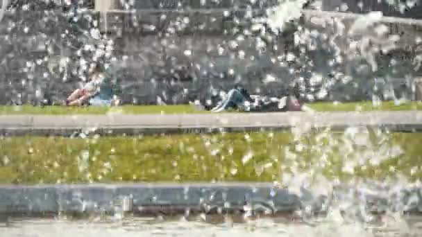 喷喷泉与绿色的草坪和几个人躺在和坐在春天的飞溅喷泉与水晶珠水和放松的年轻人在比利时的绿色草坪上春天 — 图库视频影像