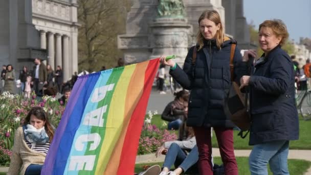 ブリュッセル ベルギー 2019年3月30日 スロモの建物で緑の芝生の上にペースという言葉で虹のバナーを保持する2人の女性活動家の印象的な眺め — ストック動画