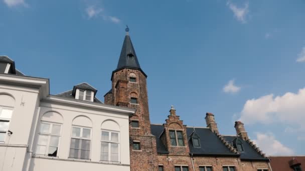 スローモーションで晴れた春にベルギーのブルージュの塔を持つ歴史的な建物スロモで春の青空と晴れた日にベルギーのブルージュの高い塔を持つ古いレンガ造りの建物の美しい景色 — ストック動画