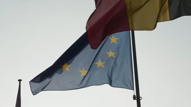比利时和欧盟的横幅在春天的阳光明媚的天旗杆上飘扬 在缓慢的春天里 在缓慢的春天里 在一幅巨大的比利时三条纹国旗和一面蓝色的大横幅上飘扬在旗杆上 — 图库视频影像
