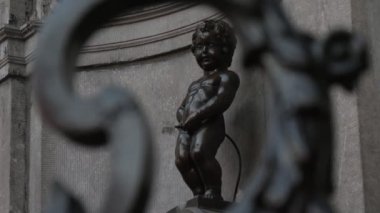 Brüksel, Belçika - 1 Nisan 2019: Brüksel'in ünlü simgelerinden Belçika'daki 'Little Pisser' bronz heykelinin muhteşem manzarası, slo-mo'da bir çitin içinden vuruldu 