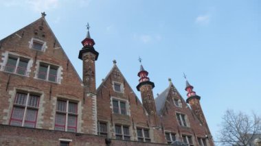 İlkbaharda Brugge'de yüksek kuleleri ve üçgen çatıları ile Ortaçağ binası Yüce çan kuleleri ve hava vanes, üçgen çatılar ve ilkbaharda bir kanal geniş pencereler ile Etkileyici Ortaçağ binası