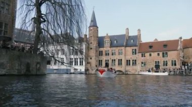 Ortaçağ binalarıngüneşli bir gün Fairylike görünümünde birçok tarihi binaları ile Brugge Hızlı yüzen motorbot, taş kanal banka, ilkbaharda Brugge yüzen bir motorboat gelen turistler ile başka bir motorbot