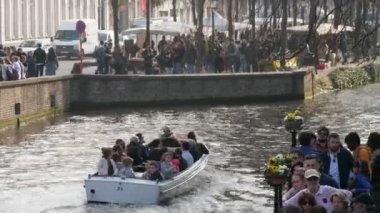 Brugge, Belçika - 2 Nisan 2019: Güneşli bir günde Brugger'de birçok insanla birlikte tarihi bir kanalda hızlı bir motorlu teknede hareket eden bir grup turistin neşeli görüntüsü 