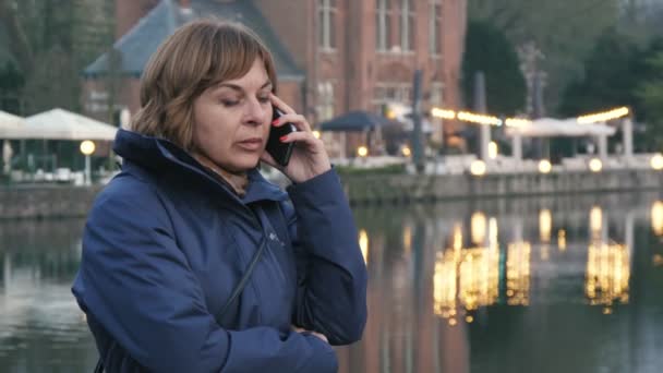 Doordachte Vrouw Praten Telefoon Met Verlichte Huizen Achter Brugge Origineel — Stockvideo