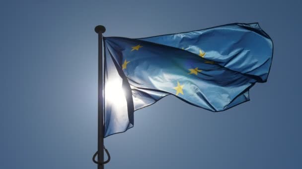 飘扬的欧盟旗帜与十二颗金色的星星在日落时分在懒洋洋的欧盟国旗与蓝色背景的欧盟旗帜和十二颗金色的星星在灿烂的日落中缓慢移动 — 图库视频影像