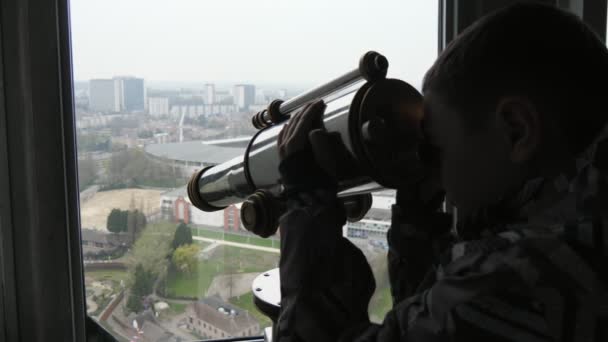 小男孩在阳光明媚的一天从比利时一座高楼看望远镜 一个穿着五颜六色夹克的小男孩在比利时春天欣赏风景如画的城市景观和现代建筑和公园 — 图库视频影像
