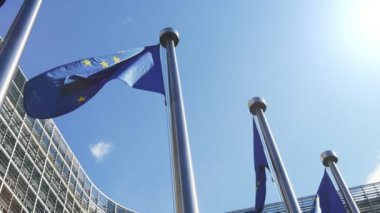 Slo-mo'da güneşli bir günde Avrupa Komisyonu'nda dalgalanan gururlu Ab bayrakları Slo-mo'da ilkbaharda yüksek modern ve camsı resmi evde dalgalanan mavi arka planlar ve altın yıldızlarla Avrupa standartlarının görünümüne inin 