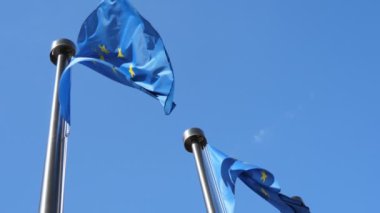 Slo-mo'da göksel gökyüzünde metalik bayrak direkleri üzerinde çırpınan iki ciddi Ab afişi Brüksel'de ilkbaharda yavaş çekimde açık mavi gökyüzünde metalik bayrak direkleri üzerinde sallanan iki gururlu Ab bayrağının görünümünden aşağı güzel