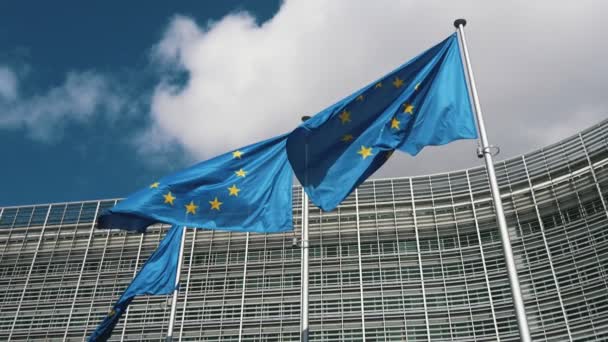 春の欧州委員会ビルの旗柱に3枚のEuの旗が掲げられており 青い背景を持つ3つの欧州連合の旗と スロモのブリュッセルのセレステ空を陽気に飛ぶ星の眺め — ストック動画