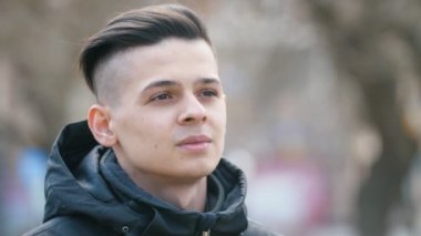 Yakışıklı genç adam kenara bakıyor ve baharda parkta geleceği düşünüyor Kısa saç kesimi ile düşünceli bir erkek öğrencinin etkileyici görünümü baharda bir parkta güvenle bir kenara bakıyor
