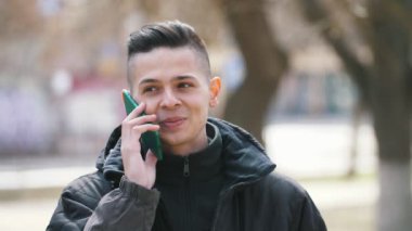 Akıllı telefon da konuşan ve baharda bir ara sokakta gülümseyen genç adam şaka siyah ceketli akıllı bir genç adamın komik görünümü gülümseyerek, şaka, baharda bir parkta neşeyle onun akıllı telefon konuşurken