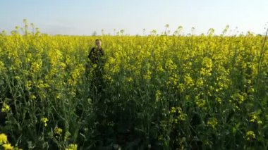 Neşeli çocuk yavaş çekimde yaz aylarında güzel bir kolza tarlasında koşuşturan kot pantolon ve siyah gömlekli enerjik on yaşındaki bir çocuğun iyimser görünümü yaz aylarında slo-mo'da çiçek açan kolza tohumu alanından geçiyor.