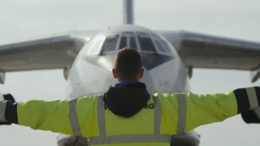 Kiev, Ukrayna - 26 Haziran 2018: Aerodrome'da turuncu çubukları yükseltip geçerek büyük bir uçağa jest gösteren sarı üniformalı bir trafik kontrolörünün heyecan verici görünümü