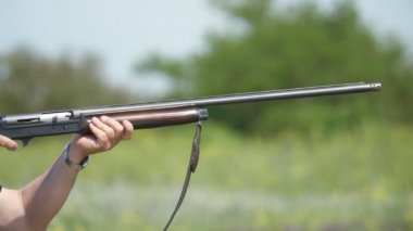Kil güvercinlere ateş eden adam ve slo-mo'daki gecikan bir adamın geveci yakın çekiminde, tek namlulu tüfeğini tutan ve skeet güvercinlerine ateş eden adam, yazın slo-mo'da uçuşan skeet güvercinlerine ateş ediyor.
