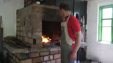 Erimiş metalik bir çubuk bakarak ve bir demirci şekillendirmek için planlar bir dövme demir gül düşünme genç bir demirci geleneksel demirci heyecan verici görünümünde el yapımı öğeleri yapma bir önlük genç adam