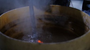 El yapımı gül bir demirci atölyesinde erimiş demir soğutmak için balmumu ile balmumu ile büyük bir yuvarlak tencereye koymak bir gül demir eski bir demirci Fairylike görünümünde soğutmak için balmumu ile bir tencereye konur. Buhara yol açar..