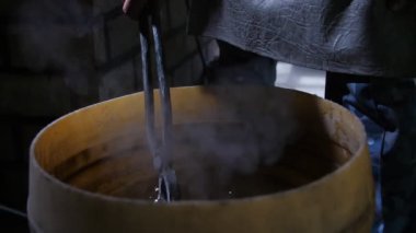 Demir gül bir atölyede kalitesini mükemmelleştirmek için balmumu ile bir tencereye yerleştirilir Bir demirci atölyesinde erimiş çelik soğutmak için balmumu ile büyük bir yuvarlak tencereye koymak bir gül demir çarpıcı görünümü. İlham verici görünüyor..