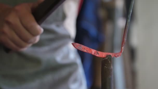 穿着围裙的年轻人在传统的铁匠造型中塑造手工制作的商品 一个年轻的铁匠看着一根熔融的金属棒 想着一朵锻铁玫瑰 他计划在铁匠身上形成 — 图库视频影像