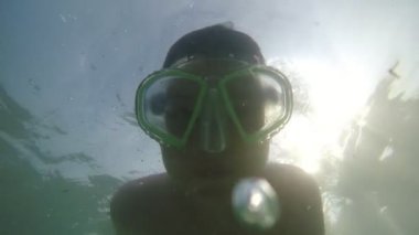 Gözlükle su altında yüzen ve slo-mo'da kameraya gülümseyen neşeli çocuk maskeli küçük bir çocuğun sualtı dalışı yapıp yaz aylarında alanya sahilinde yavaş çekimde hayatının tadını çıkarıyor.