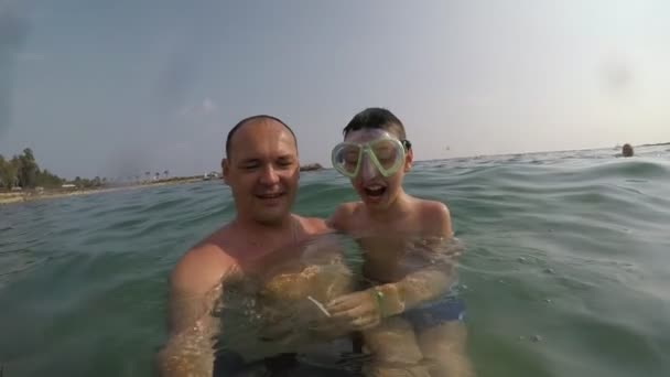 陽気な少年と彼の父親は スロモで夏のターリーの海の波で笑ってマスクで彼の小さな男の子を保つ中年の男の子のスローモ楽観的な眺めでアランヤの外波で笑う — ストック動画